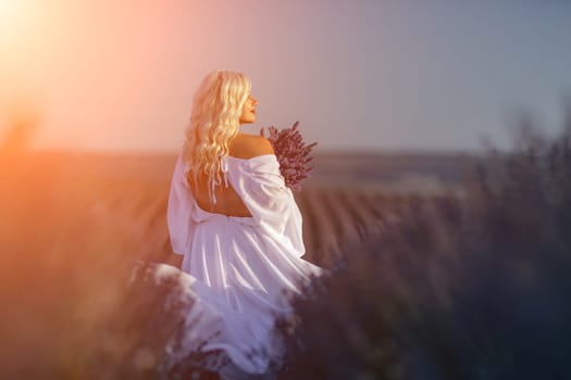 Blonde woman poses in lavender field at sunset. Happy woman in white dress holds lavender bouquet. Aromatherapy concept, lavender oil, photo session in lavender.