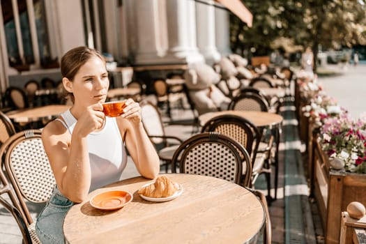 Portrait of happy woman sitting in a cafe outdoor drinking coffee. Woman while relaxing in cafe at table on street, dressed in a white T-shirt and jeans.