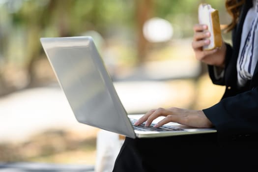 Cropped shot businesswoman sitting on the bench in city park and using laptop.