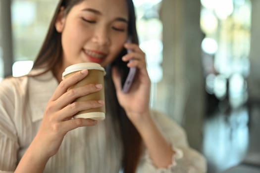 Smiling businesswoman holding paper cup of coffee and talking on mobile phone.