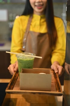 Friendly female waitress serving matcha green tea and cake in a cardboard takeaway box to customer.