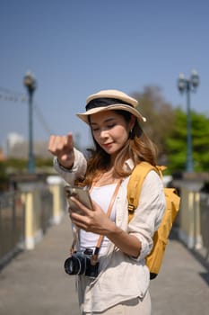 Female tourist searching direction on smart phone while sitting on bridge over river.