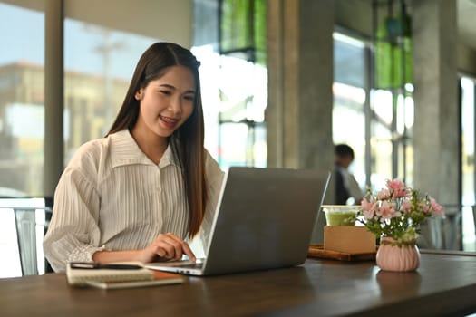 Smiling businesswoman using laptop on wooden table at coffee shop during working remotely.
