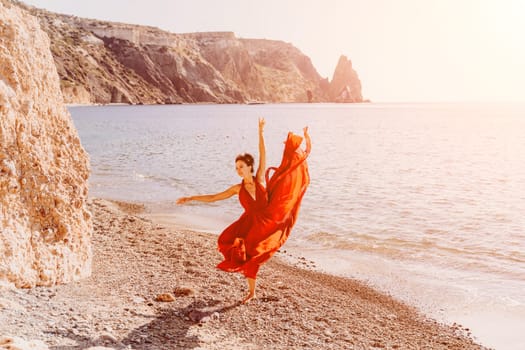 Woman red dress sea. Female dancer in a long red dress posing on a beach with rocks on sunny day. Girl on the nature on blue sky background