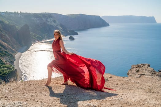 A woman in a red flying dress fluttering in the wind, against the backdrop of the sea