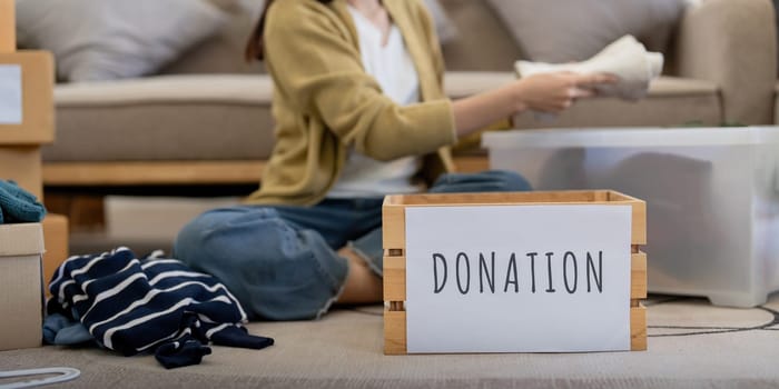 Donation, asian young woman sitting pack object at home, putting on stuff into donate box with second hand clothes, charity helping and needy people. Reuse recycle.