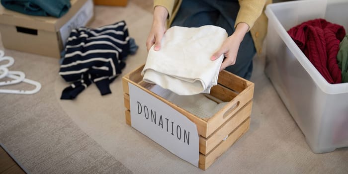 Donation, asian young woman sitting pack object at home, putting on stuff into donate box with second hand clothes, charity helping and needy people. Reuse recycle.