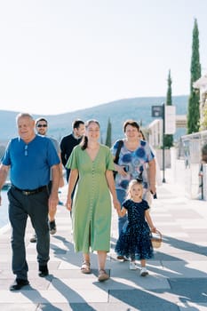 Adults with a little girl in a witch costume with a basket walk down the street. High quality photo