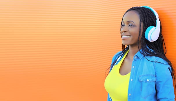 Portrait of young african woman listening to music in headphones on orange background