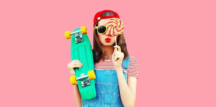 Summer portrait of young woman with lollipop and green skateboard on pink background