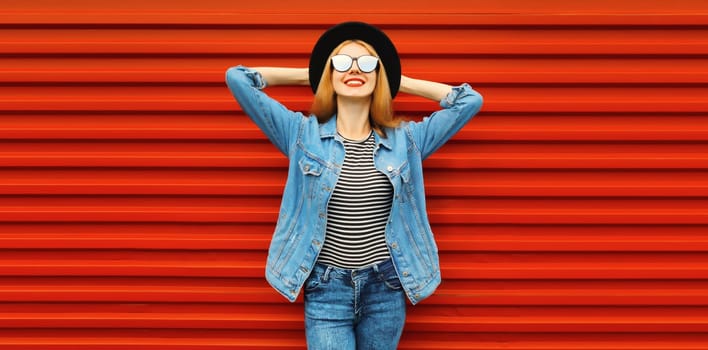 Portrait of stylish modern smiling young woman wearing denim jacket, black round hat on red background