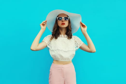 Beautiful caucasian young woman model posing wearing white summer straw hat on blue studio background