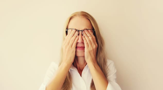 Tired overworked middle-aged woman employee rubbing her eyes suffering from eye strain, dry eye syndrome or headaches after working at the computer