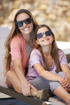 Portrait, love and mother on vacation with daughter outdoor in sunglasses for summer, travel or holiday. Family, smile and mom hugging girl child on poolside deck chair for bonding, trip or getaway.