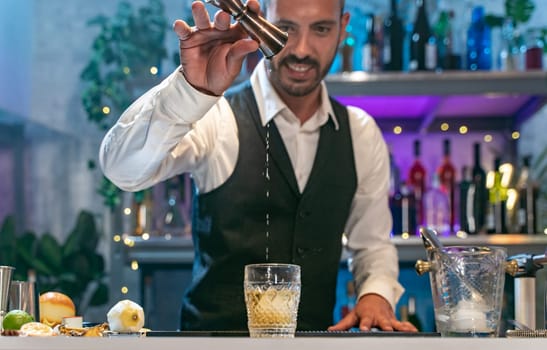 Expert barman in a white shirt and black apron smiling happy making cocktail at party in nightclub. Nigh life. High quality photo