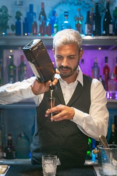 Professional barman in a white shirt and black apron making cocktail at party in nightclub. Nigh life. High quality photo
