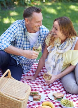 Couple, picnic and alcohol for bonding in outdoor nature, love and romance in relationship on weekend. Wine glasses, conversation and people on date in countryside, adventure and forest for happy.