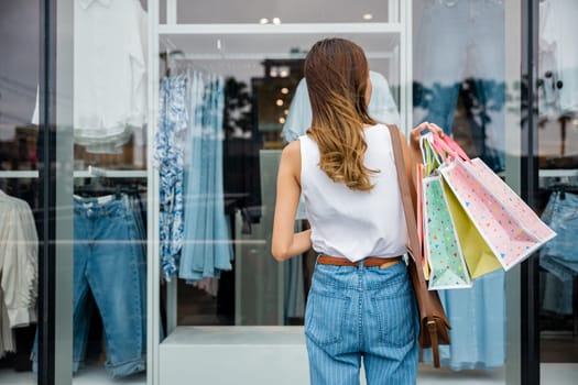 A stylish young woman with shopping bags on the sidewalk in front of a fashion store window. She's enjoying her day out shopping and finding great deals.
