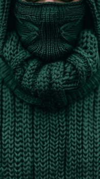 A person wearing a green sweater and glasses with their face covered