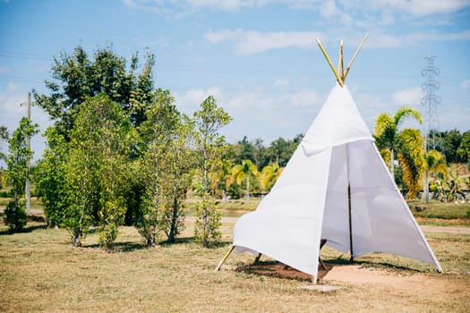 A charming summer wedding teepee stands in a green field evoking joy and celebration. The traditional wigwam adorned with dreamcatcher decorations creates a picturesque scene of family happiness.