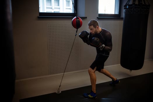 Determined concentrated boxer practicing coordination and punch control on red and black floor-to-ceiling bag during intense workout in modern gym