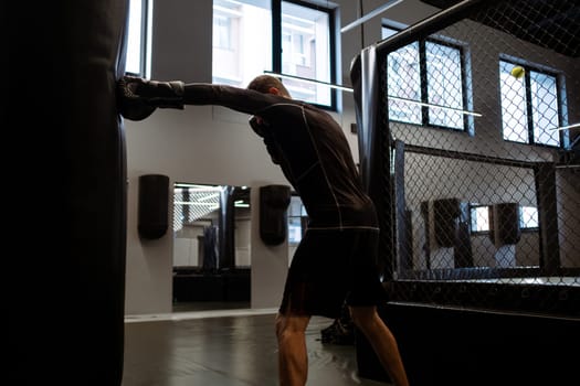 Determined adult man in sportswear and boxing gloves training with heavy bag in gym. Concept of cardiovascular high-intensity, full-body workout to burn calories, build muscle, and improve endurance