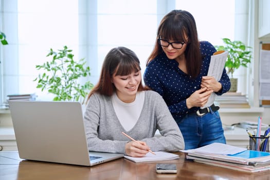 Teenage student studying at desk with computer, teacher trainer mentor helping teaching. Education, teaching, youth concept