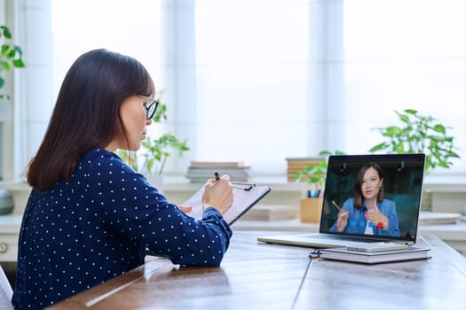 Mature woman talking online with young female using video call chat conference. Middle aged female working remotely in home office with patient, client, colleague, student on laptop computer screen