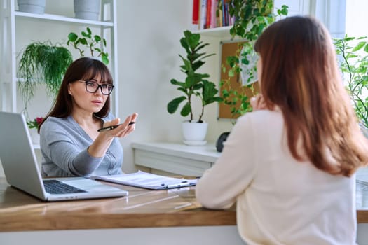 Middle-aged female psychologist, psychotherapist, counselor, social worker working with young woman patient. Psychology therapy professional help consultation treatment support mental health concept