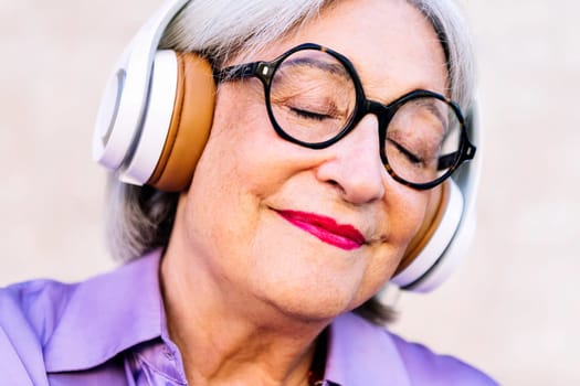 close up portrait of a smiling senior woman with eyes closed enjoying listening to music in headphones, concept of elderly people leisure and active lifestyle