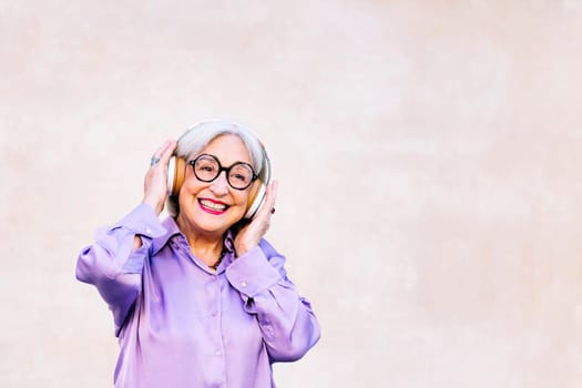 funny senior woman smiling happy listening to music on her headphones, concept of elderly people leisure and active lifestyle, copy space for text