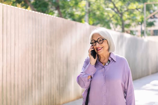 beautiful senior woman smiling happy while walking on the street talking on the phone, concept of technology and elderly people leisure, copy space for text