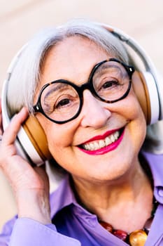 close up portrait of a smiling senior woman looking at camera enjoying listening to music in her headphones, concept of elderly people leisure and active lifestyle