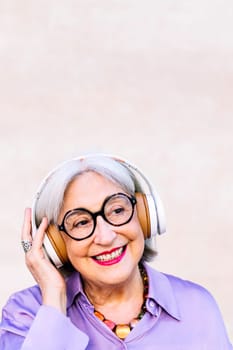 smiling senior woman in glasses listening music in her headphones, concept of elderly people leisure and active lifestyle, copy space for text