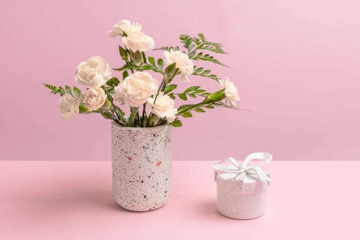 Bouquet of white carnations in a vase and a gift box on the pink background.