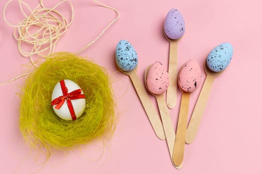 Colored Easter eggs with wooden spoons and a nest on the pink background. Top view.