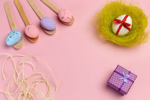 Colored Easter eggs on wooden spoons, a nest and a gift box on the pink background. Top view.
