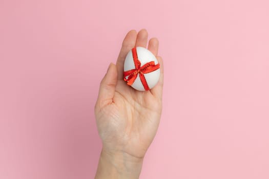Woman is holding the Easter egg tied with a red ribbon on the pink background. Top view.