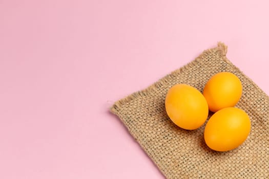 Yellow Easter eggs on the sackcloth bag with the pink background. Top view with a copy space.