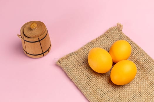 Yellow Easter eggs on the sackcloth bag with the pink background. Top view with a copy space.