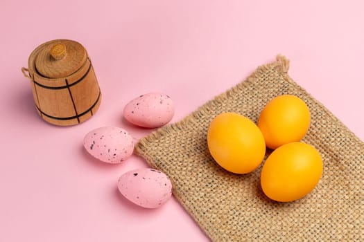 Colored Easter eggs on the sackcloth bag and the pink background. Top view.