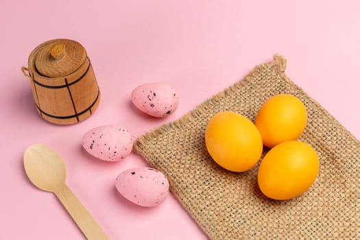 Colored Easter eggs and wooden utensils and cutlery with the pink background. Top view.