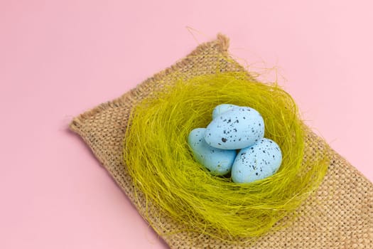 Nest with colored Easter eggs on the sackcloth bag with the pink background. Top view.