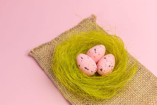 Nest with colored Easter eggs on the sackcloth bag with the pink background. Top view.