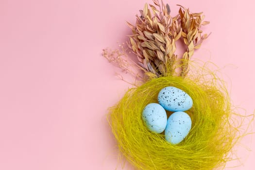 Nest with colored Easter eggs on the pink background with decor plants. Top view.