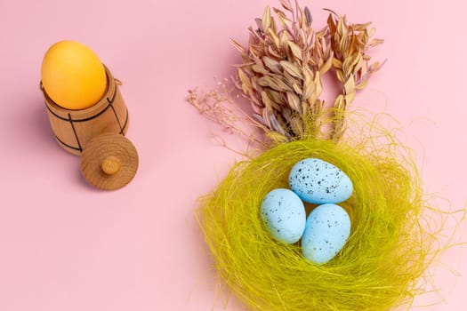 Nest with colored Easter eggs on the pink background with decor plants and wooden utensil. Top view.