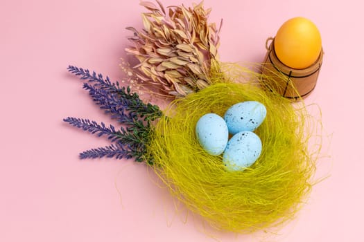 Nest with colored Easter eggs on the pink background with decor plants and wooden utensil. Top view.