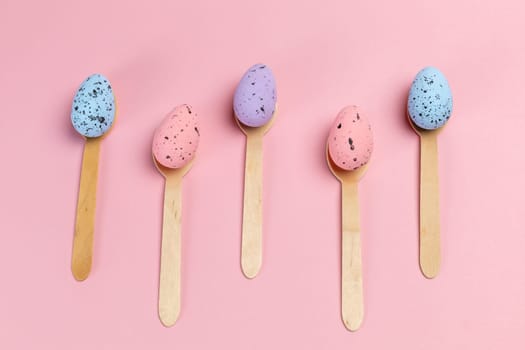 Colored Easter eggs with the wooden spoons on the pink background. Top view.