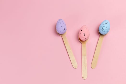 Colored Easter eggs with the wooden spoons on the pink background. Top view.