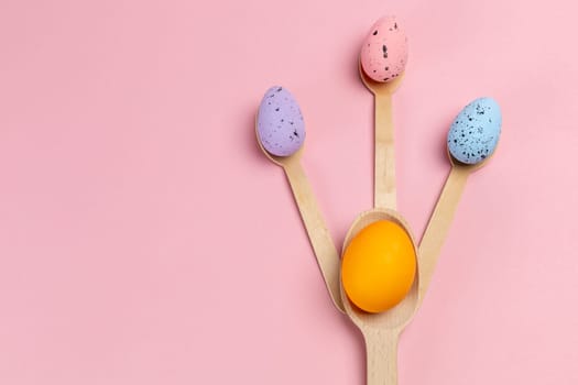 Colored Easter eggs with the wooden spoons on the pink background. Top view.